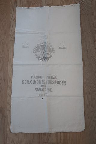 Gammel sæk
Tekst: "Statskontrolleret Vitaminiseret - Primol - Piller - 
Somælkstilskudsfoder til smågrise - 25 kg"
96cm x 53cm
God stand
Vi har et godt udvalg af gamle sække både med og uden tekst