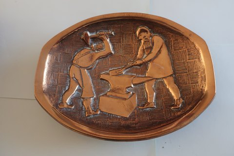 Oval platte/fad/lille skål i ædelmetal (messing)
Relief illustreret som 2 smede i arbejde
H: 13cm
B: 16,5cm
Tung
Fremstillet i Danmark