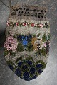 PerletaskeTaske lavet som perlebroderi med smukt mønster bl.a. blomst/rosePosefacon med snøre i toppen for kombineret lukning og "hank"Tasken har mange perler og er derfor af en væsentlig vægtL: 17cm